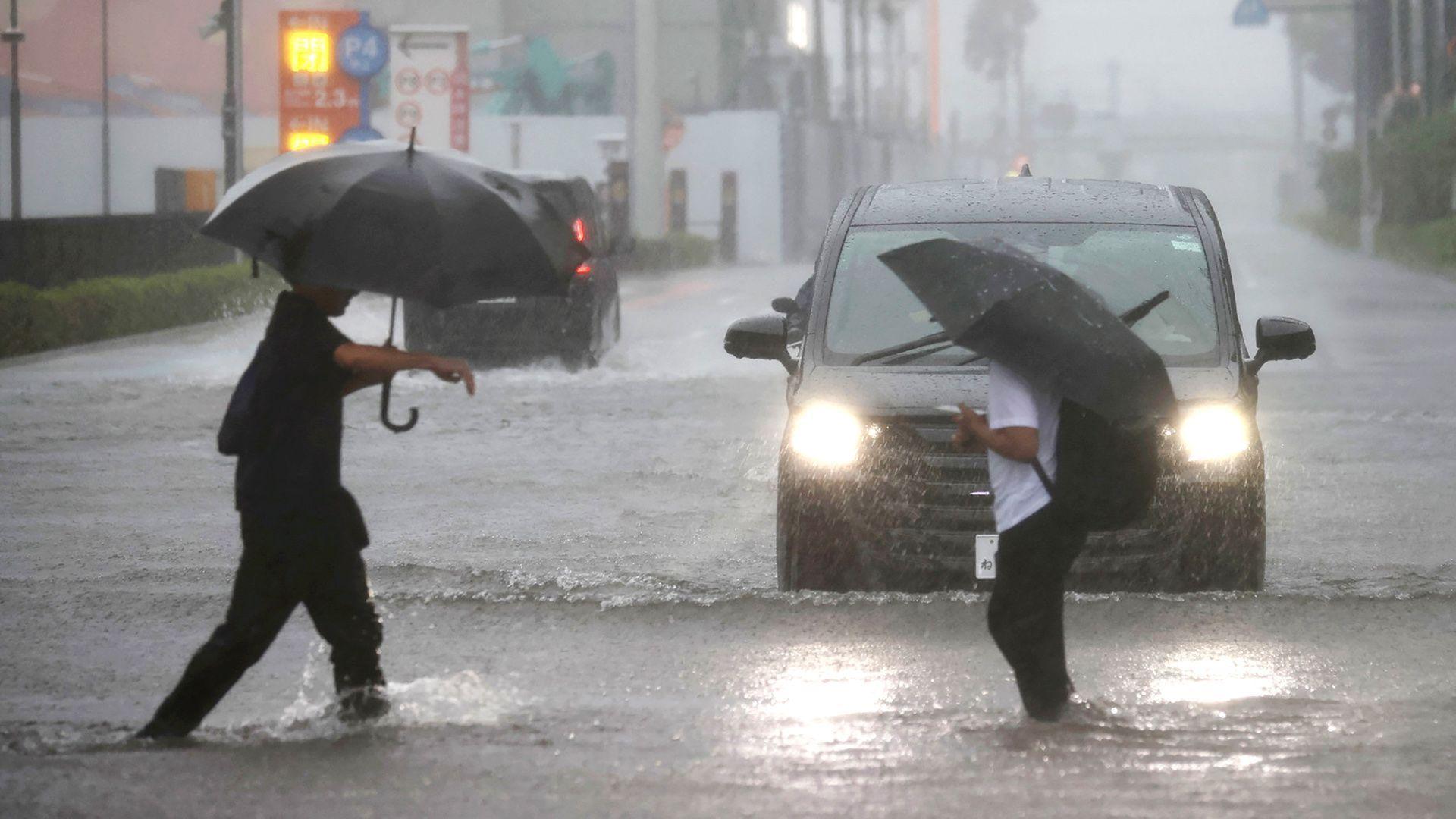 Two men with umbrellas are ankle-deep in water as they cross a road in Funabashi, Chiba Prefecture, Japan