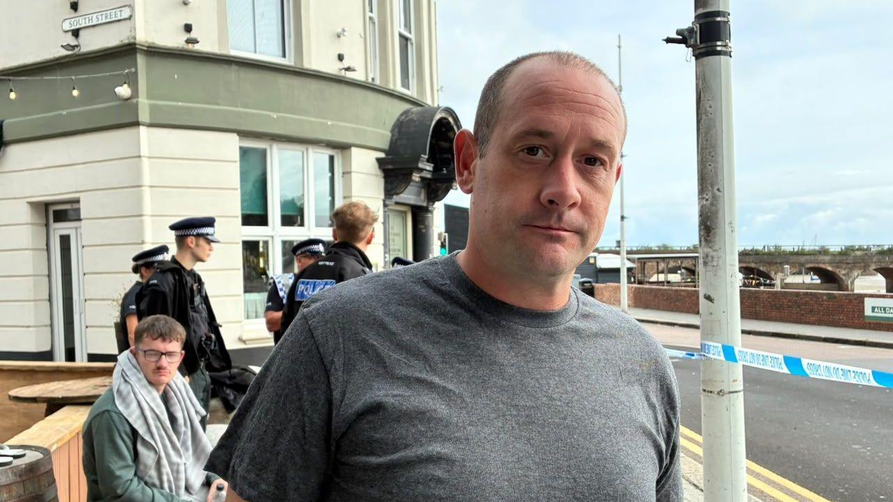 A man, Ross Honeycomb, stood by a police cordonl with police officers in the background.