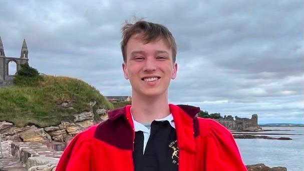 Harrison Sharples is looking at the camera and smiling. He has red Pier Walk robe on.