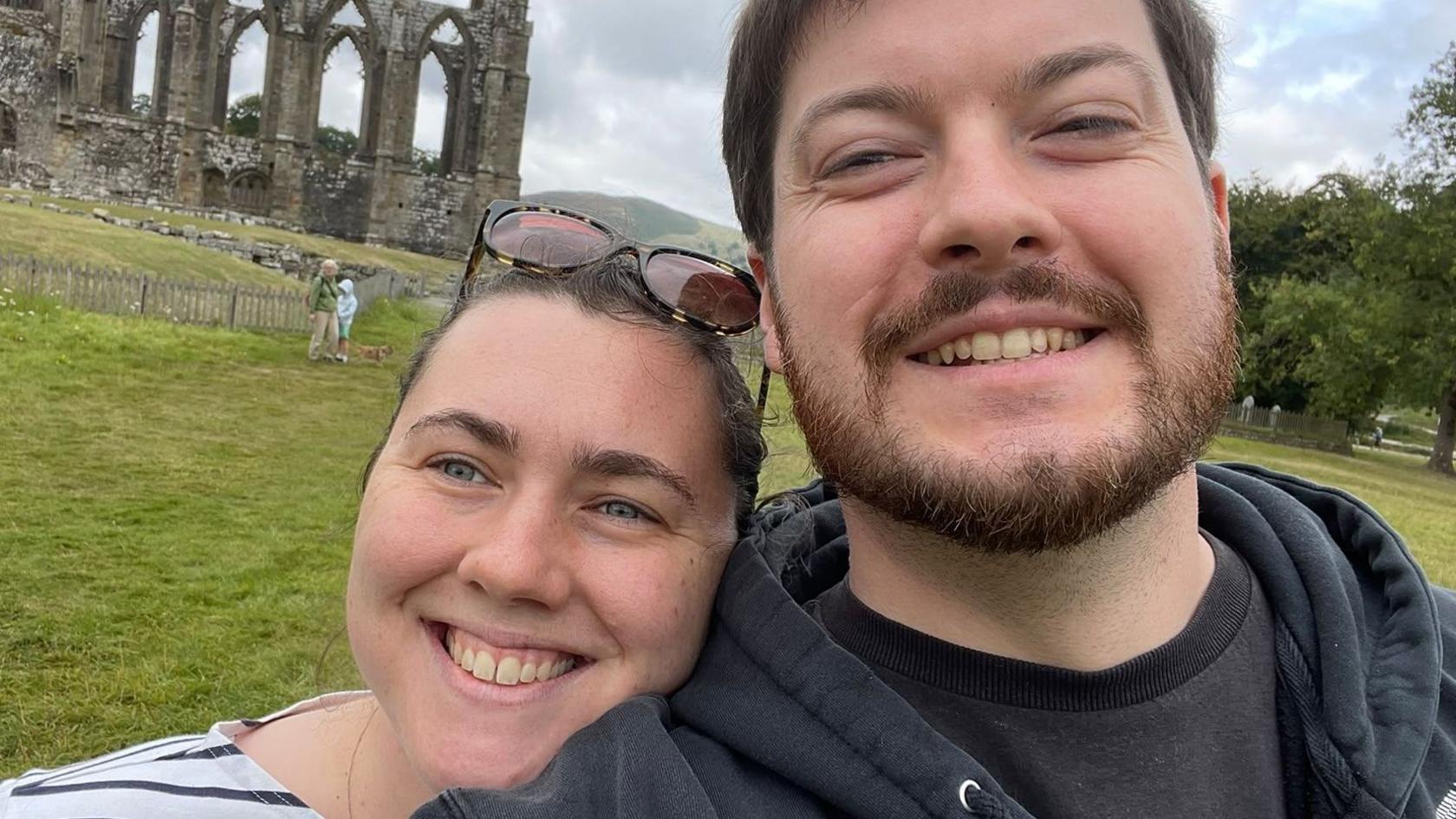 Selfie of a smiling Catie and Phil Allen standing in front of some ruins.