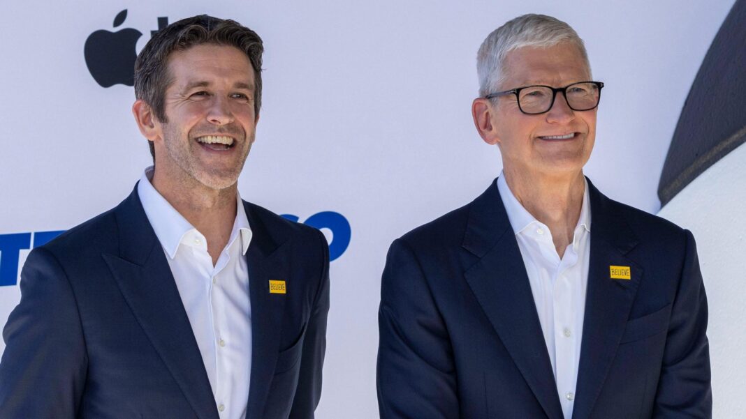 Apple's incoming chief executive John Ternus standing next to his predecessor Tim Cook. Both are smiling for cameras at an Apple event and wearing an almost identical blue blazer and white collared shirt.