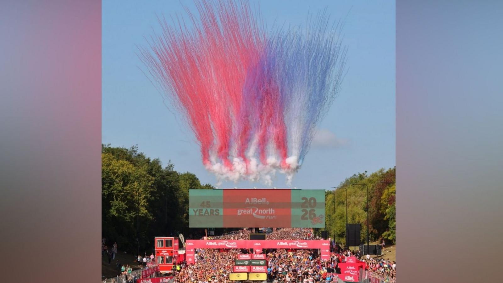 Plumes of colour fill the skies as runners cross the start line of the AJ Bell Great North Run. There are hundreds of people in running gear setting off under the red archway and down the grey tarmac road.