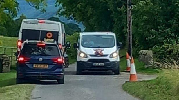 A campervan, van and car pass each other on the single track road.