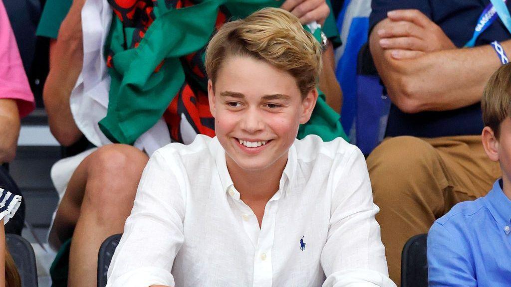 Prince George at the Commonwealth Games in August 2026. He is wearing a white shirt and smiling.