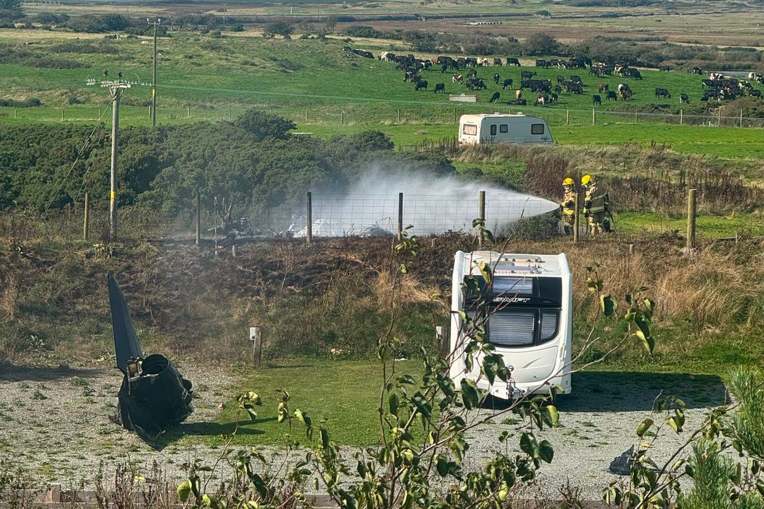 Wreckage of RAF T2 on the ground, two emergency response officers spray the wreckage with water.
