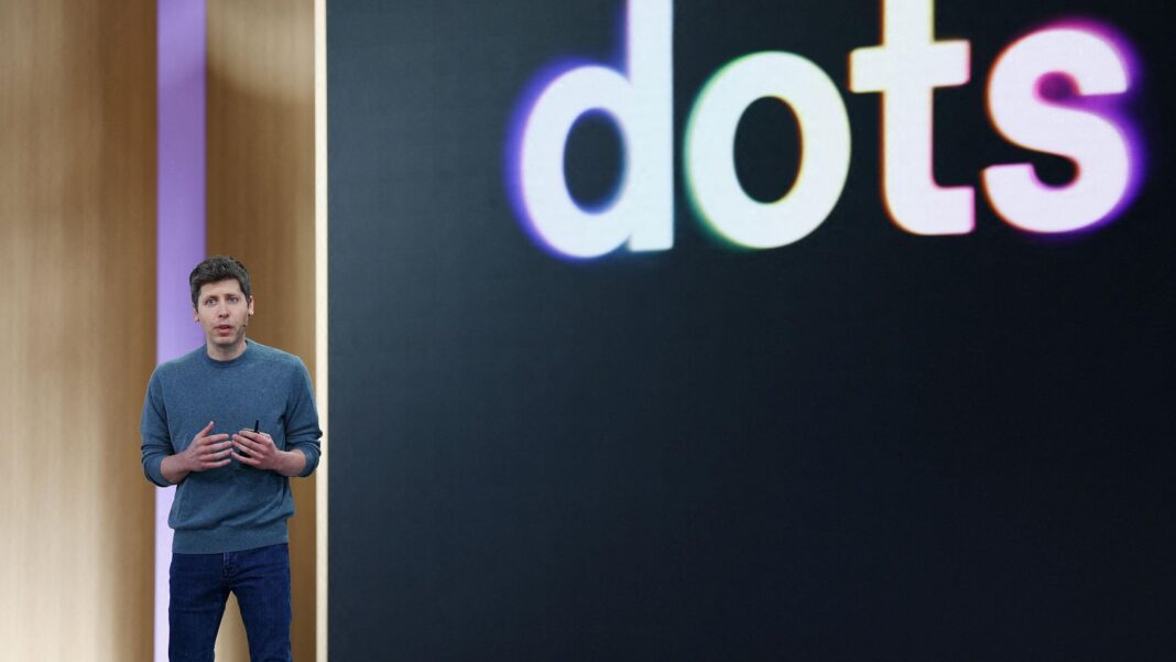 OpenAI CEO Sam Altman standing on stage at his company's annual developer conference in front of a screen with 