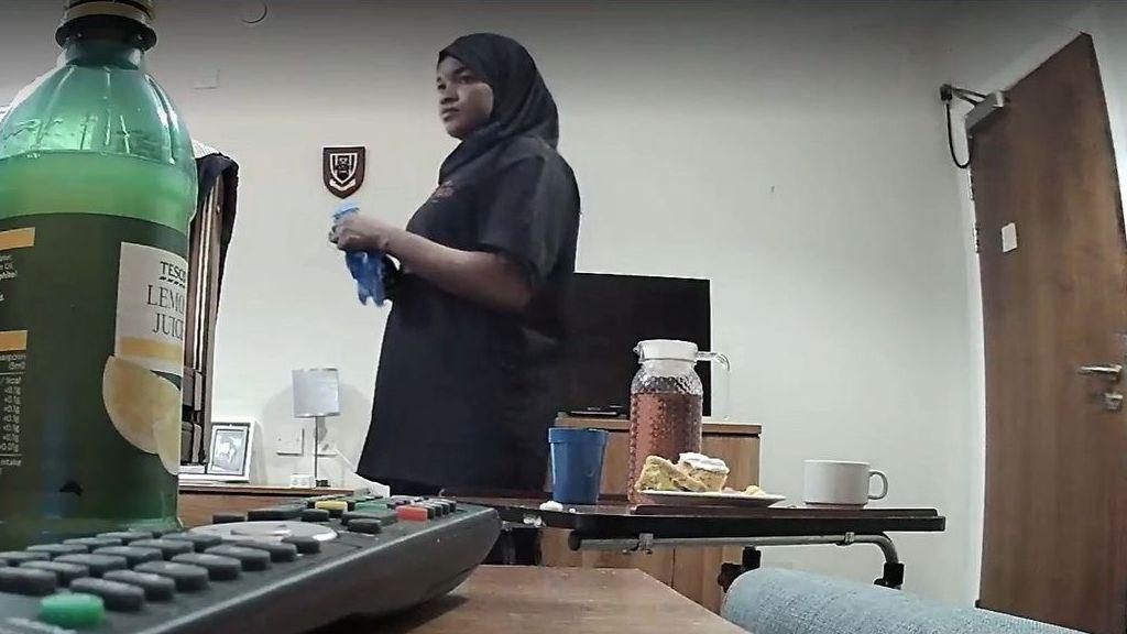 Sami is a young African woman in a black hijab in a clinical-looking room. Food can be seen on the table in front of her. The camera angle is low and looks to be set up secretly.