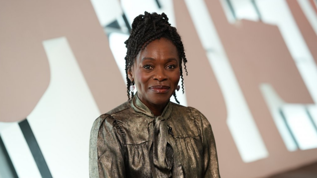 Rakie Ayola smiles towards the camera wearing a metallic top. She is sitting in front of the Wales Millennium Centre letters indoors