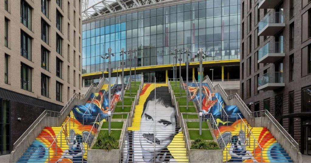 Painted steps seen from the front, with Freddie Mercury's face in black and white across the central flight and koi carp in orange and blue on the steps either side, Wembley Stadium behind