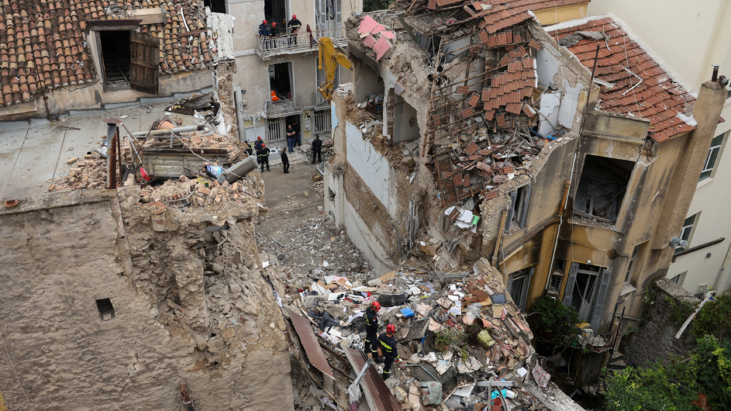 Site the blast showing the collapsed remains of the building, flanked on either side by heavily damaged properties