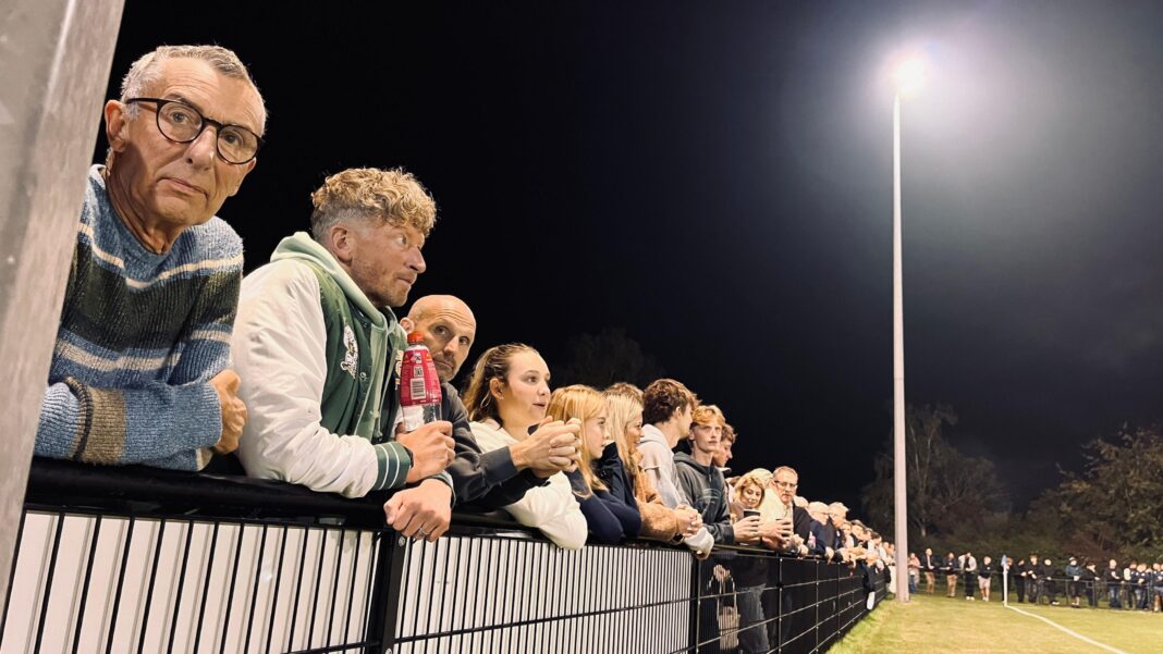 Norfolk village team triumphs in FA Cup row replay Fans stand behind a fence looking out at the pitch where the match is being played