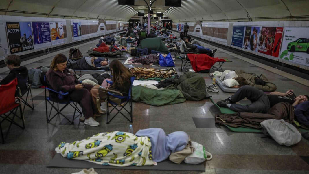 People sleeping on camping mats and sitting in fold out chairs inside a metro station during a Russian strike in Kyiv.