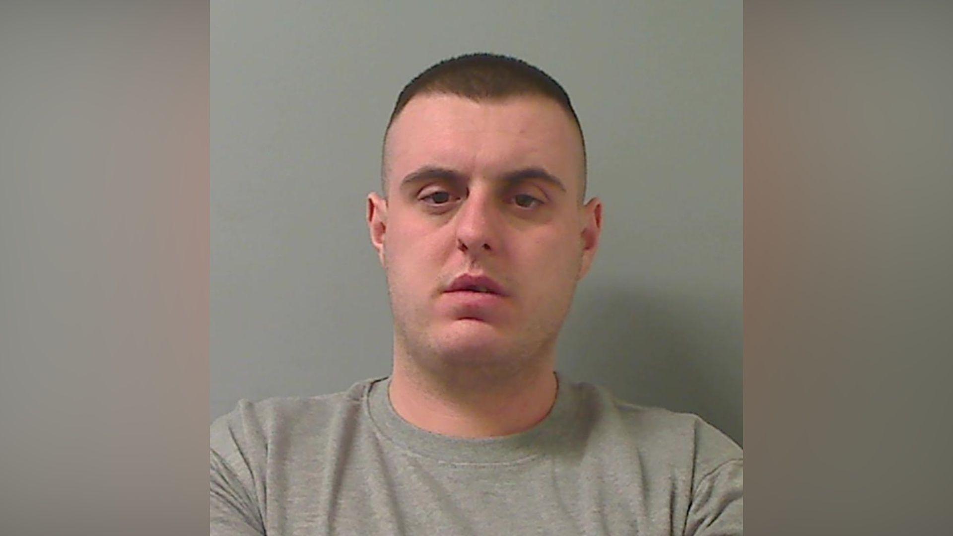 Mugshot of man with short dark hair and a grey sweater