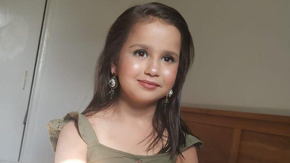A young girl wearing makeup and big earrings. She is in a green dress.
