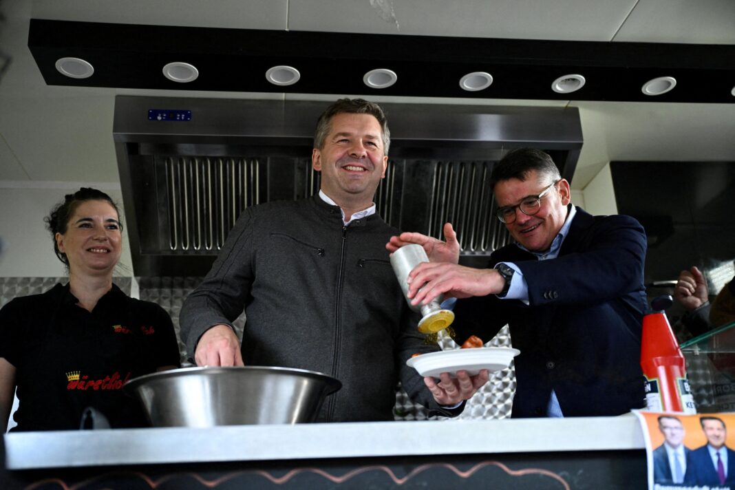 Sven Schulze (centre), together with Hesse State Premier Boris Rhein (right), serves currywurst with fries, during a campaign event in Magdeburg, Germany,
