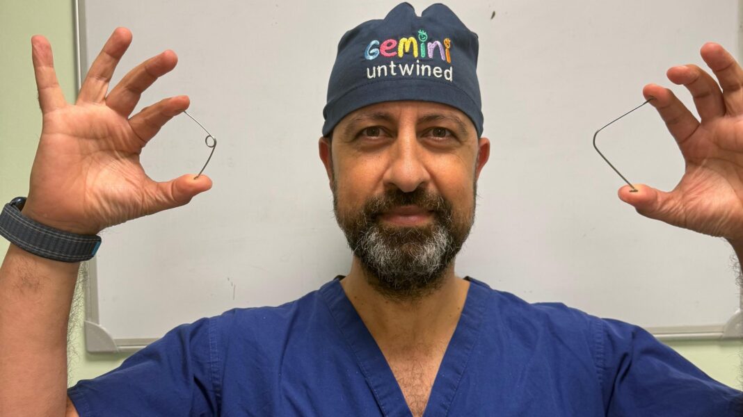 A man standing up wearing surgery scrubs and a hat holding up two metal springs.