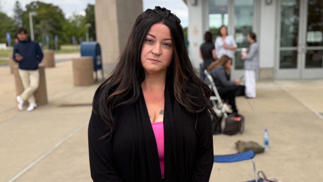 Lindsay Clancy murder trial has divided US on whether she’s victim or criminal A woman with brown hair, who wears a pink top and a black jacket, looks at the camera. People are seen blurred in the background.