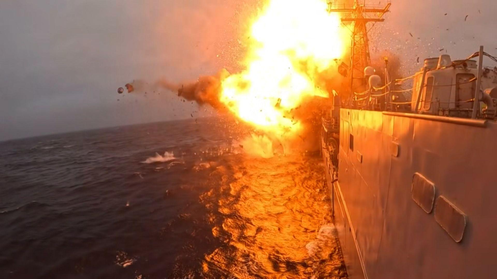 Orange flames and smokes erupts from an explosion on USS Klakring. Part of the grey warship is visible on the surface of a dark blue sea.