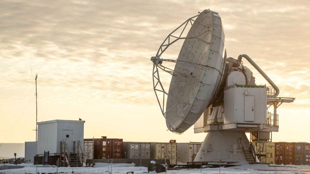 The Pituffik Space Base (formerly Thule Air Base) is pictured in northern Greenland, on October 4, 2023. It shows a large satelitte dish in front of containers, with a cloudy orange sky in the background.