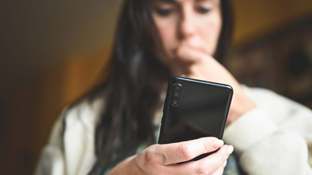 Why are there concerns AI could threaten humanity, and how real are they? A stock image of a woman looking down at her smartphone, biting her nails nervously