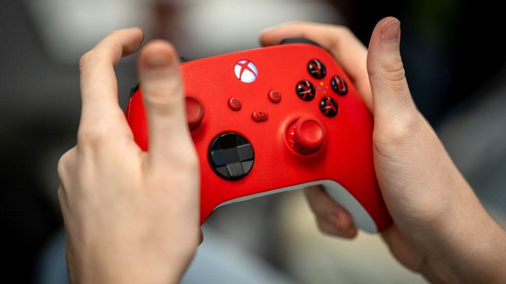 A close up of someone's hands holding a red Xbox controller