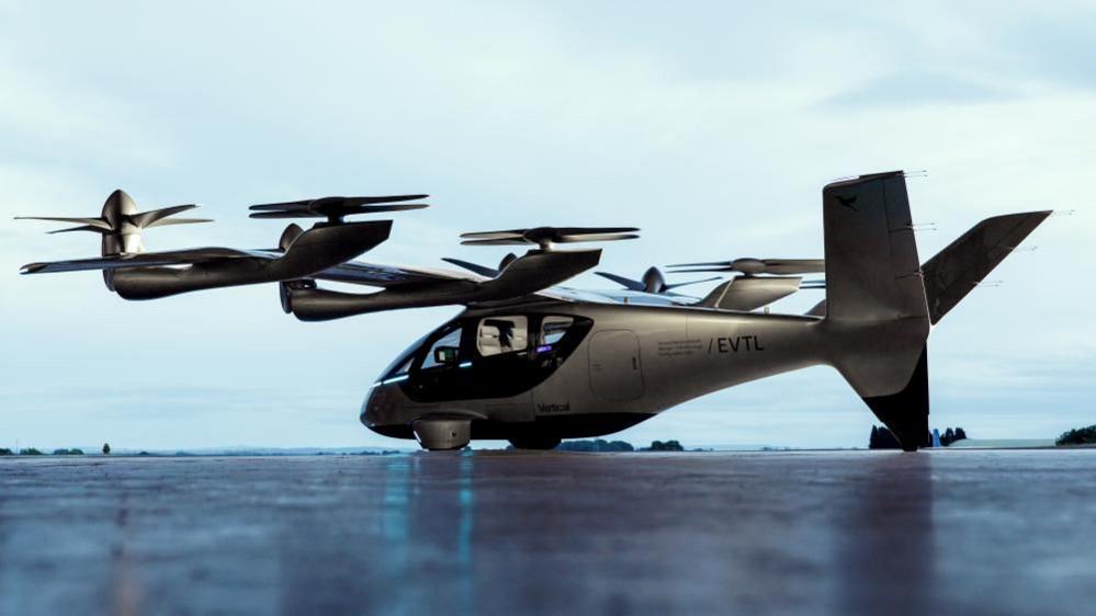 A Valo aircraft on the ground. It is silver and it has large propellers on each of its wings.
