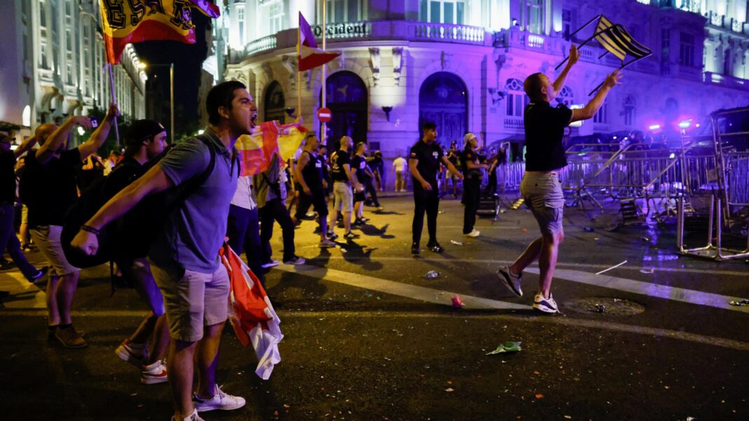 Protests in Spain over government’s handling of Ceuta migrant crisis A man shouts at police with a barricade on the right and police lights visible. Other protesters wave flags.