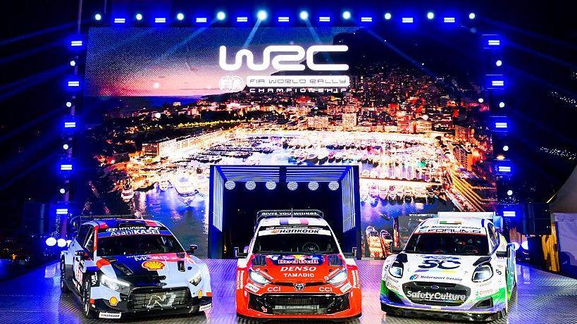 Three rally cars in front of a lit up sign featuring the World Rally Championship logo