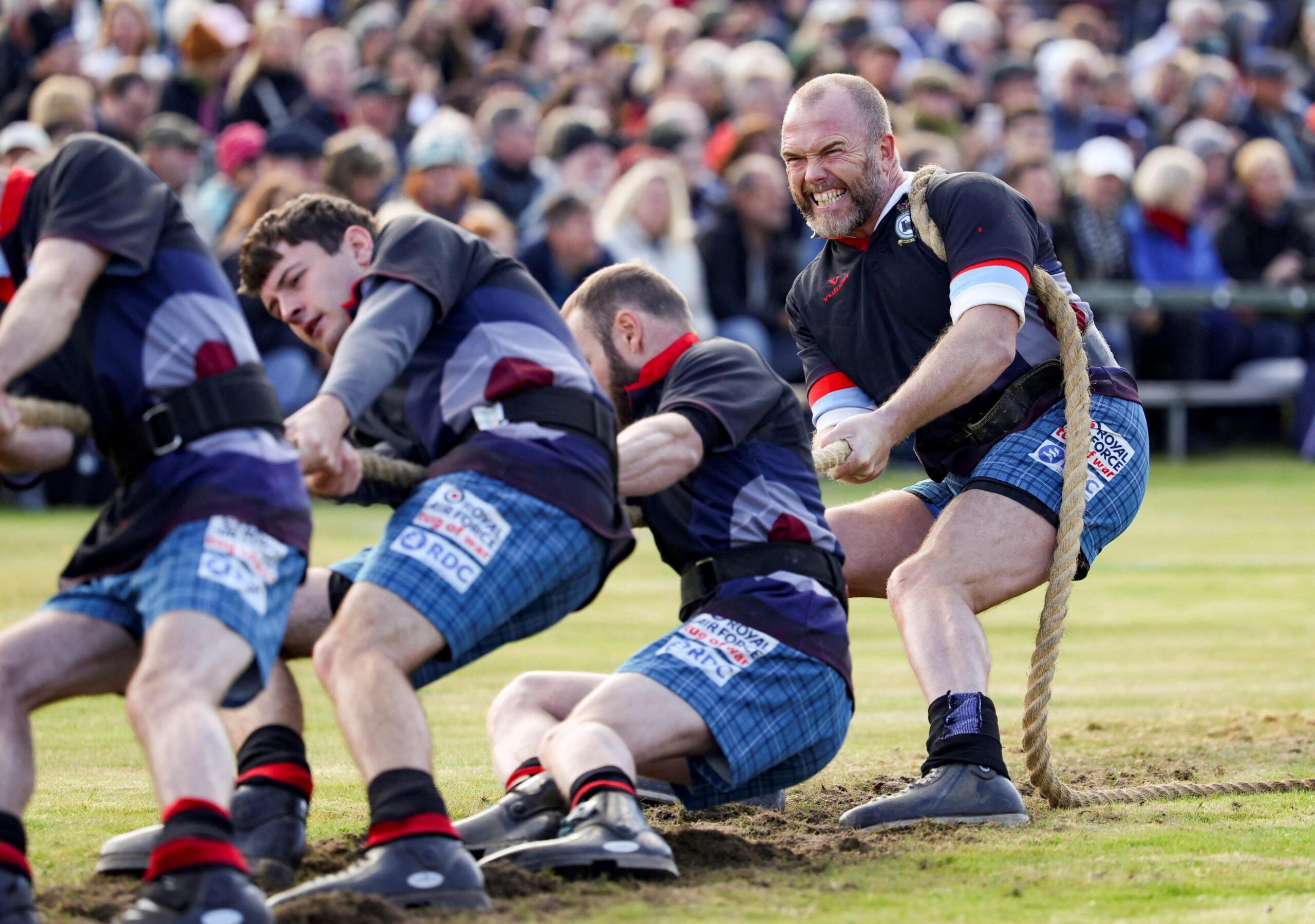 men in black tops and blue shorts pull a rope in a tug of war match