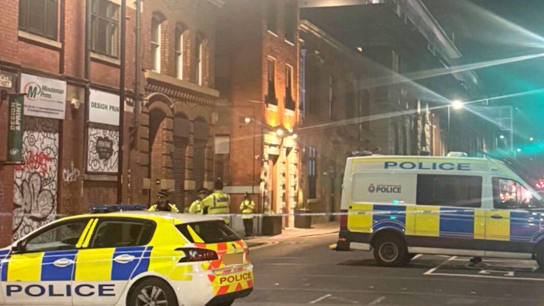 A police car and a van and several officers stand guard by a police cordon in a city-centre location.