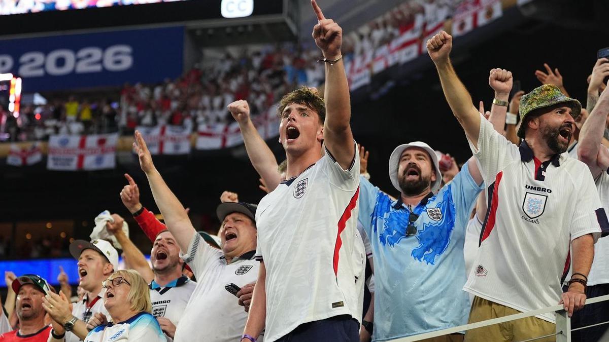 England fans wearing white retro kits singing with their arms aloft