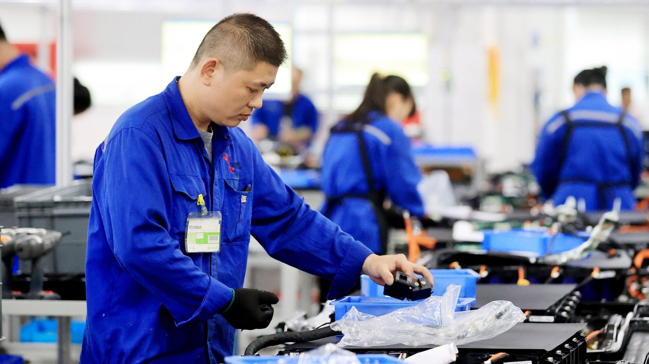 Workers in blue overalls assemble batteries for electric vehicles at a Chinese battery plant.