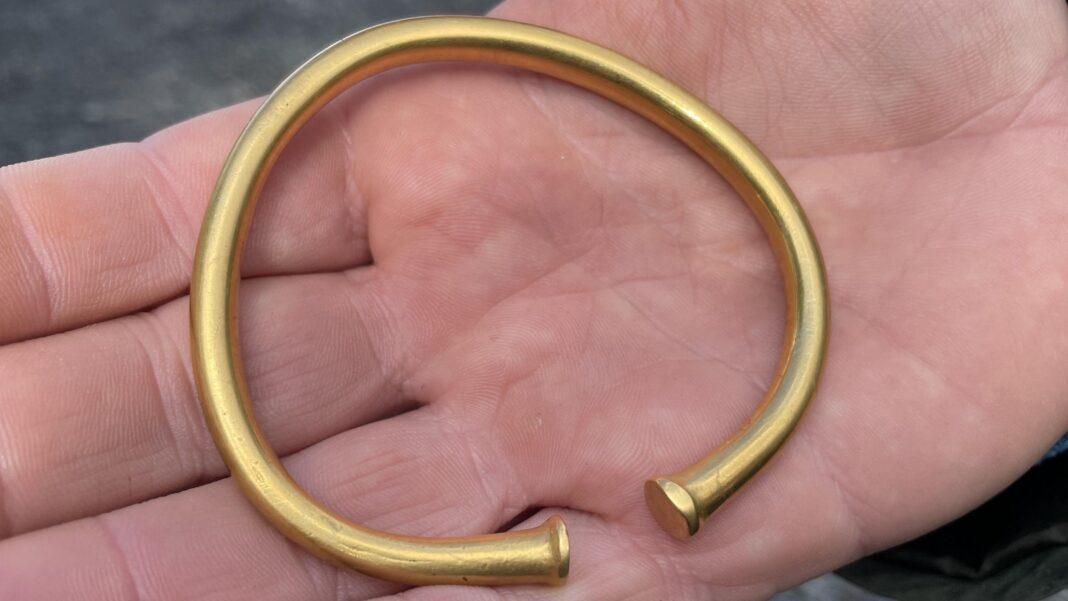 Learner drivers turn to YouTube and TikTok to cut costs – but instructors warn of risks A close-up photograph shows a gold-coloured open-ended bracelet resting across the palm of a hand. The bracelet has a smooth, rounded band with slightly flared terminals at each end and a matte metallic finish. Fine skin lines and creases in the hand provide scale, highlighting the bracelet's thickness and craftsmanship, while the blurred background keeps the focus on the circular object.