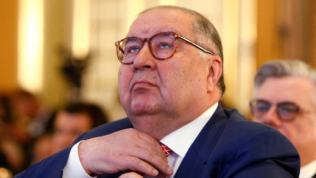 Alisher Usmanov, a middle aged man wearing glass and a dark suit, adjusts his tie while looking upwards