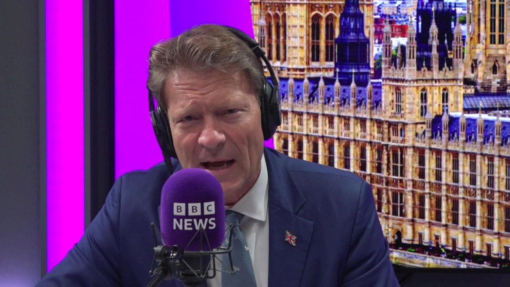 Reform UK deputy leader Richard Tice. He is sitting in a studio speaking into a purple microphone with the words BBC News on it. Behind him is a screen showing an image of the Houses of Parliament.