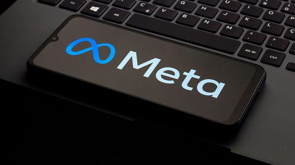 A photo of a phone kept on a laptop keyboard. The phone is displaying the logo of the company Meta