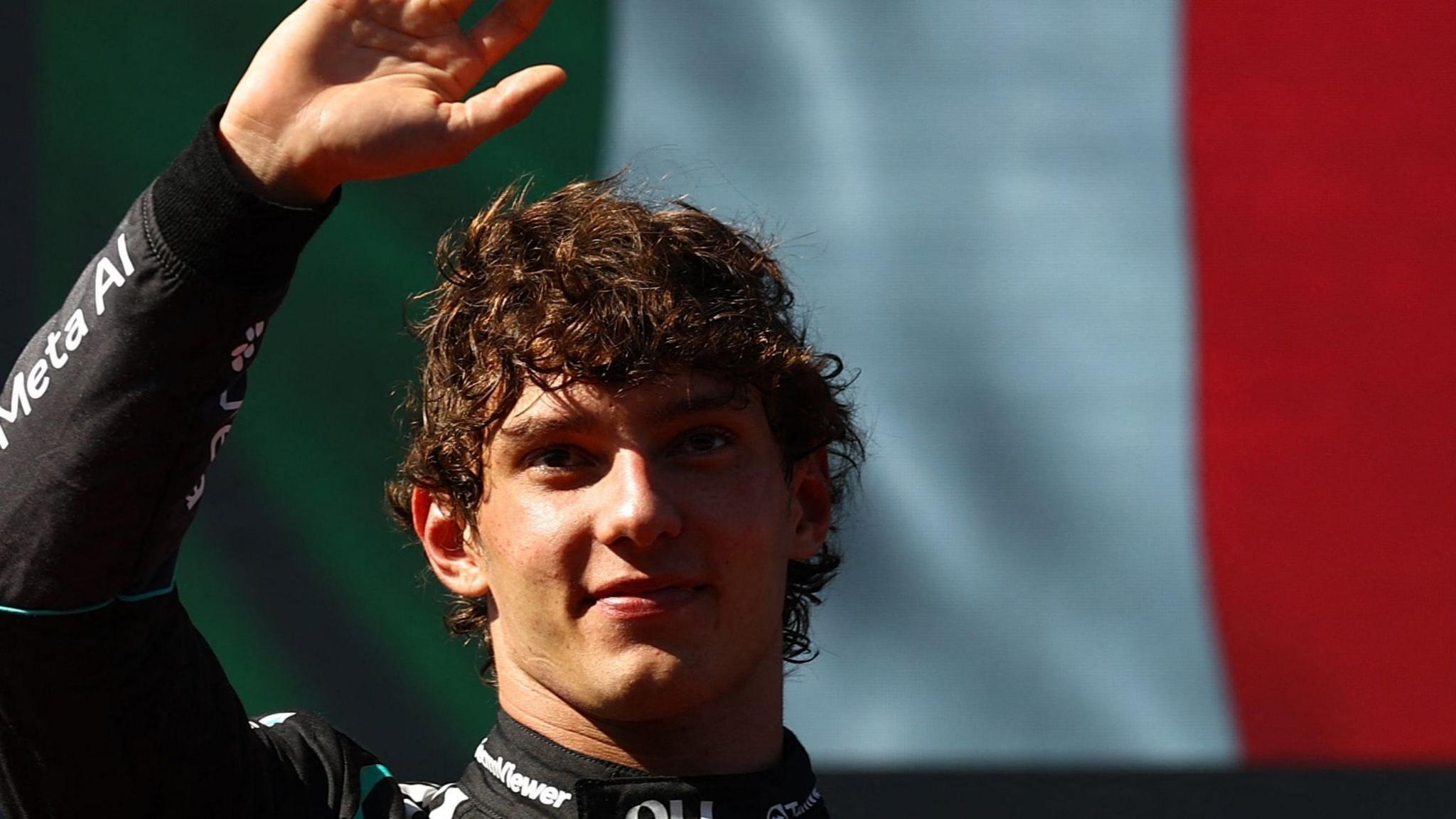 Kimi Antonelli raises his hand in celebration after winning the Spanish Grand Prix. An image of the Italian flag on a screen can be seen behind him