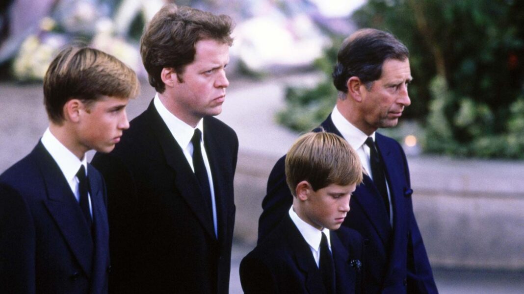 A young Prince William stands next to Earl Spencer, a young Prince Harry and Charles at Diana's funeral. They are all wearing dark suits with ties and are facing ahead solemnly.