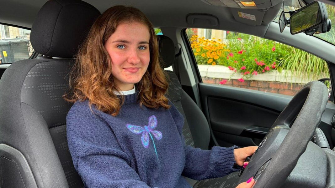 ‘Get in’ – woman joins police chase by giving officer a lift in Nissan Micra Megan sits in her car. she is smiling at the camera and has reddish to brown hair cut at her shoulders. She is wearing a blue jumper with a dragonfly on.
