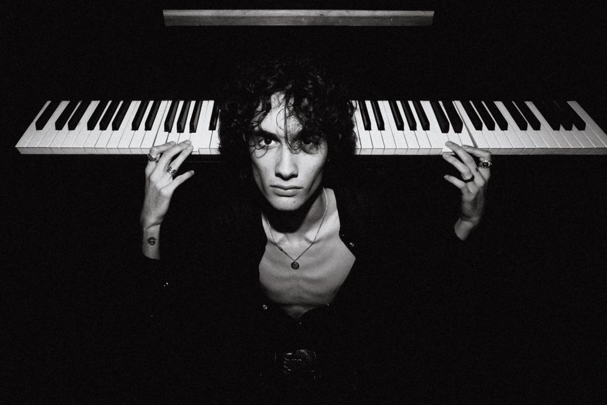 A black and white image of US singer-songwriter Sombr playing a piano backwards while looking directly into the camera