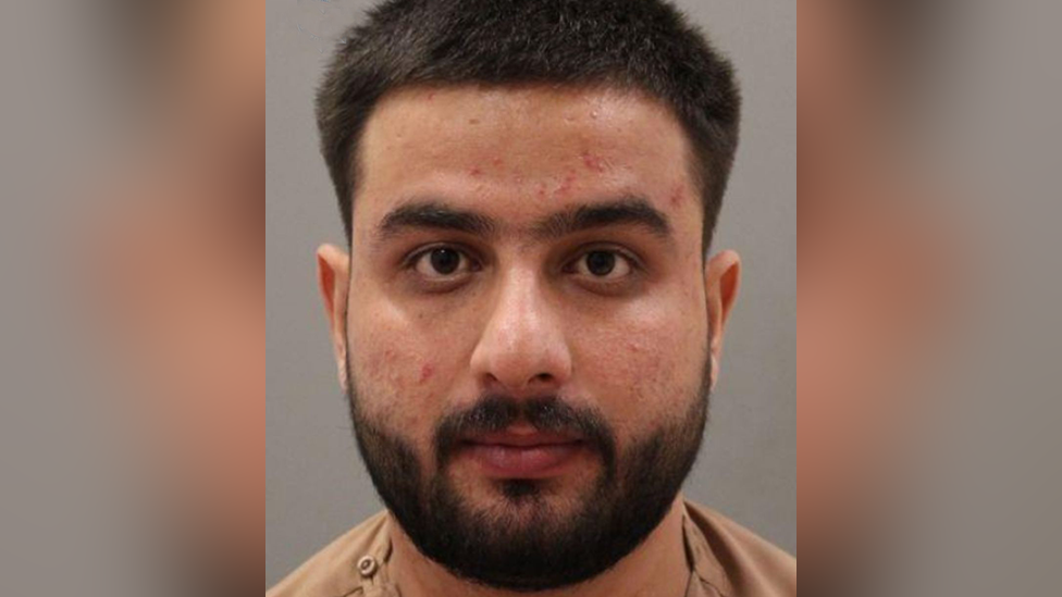 Police custody image of Sultani Bakatash. He has black hair and beard and is wearing a beige t-shirt.