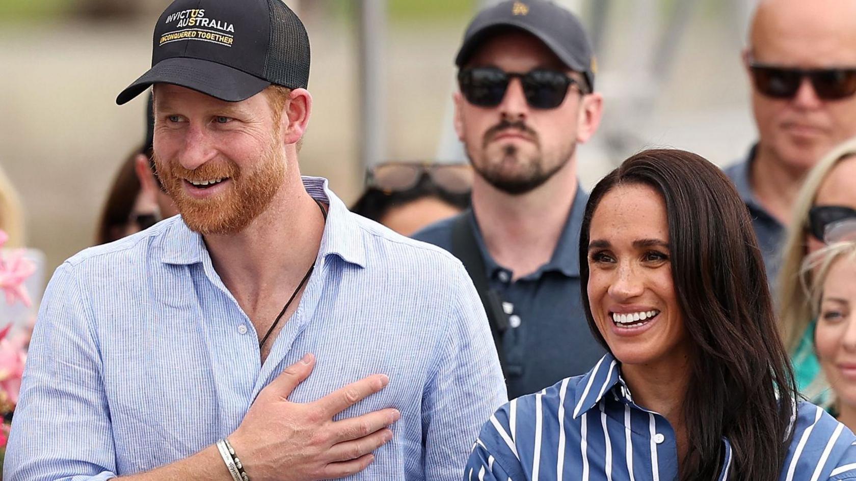 Harry and Meghan seen walking together in Sydney harbour in April. He is wearing a blue shirt and a cap, she is wearing a striped blue shirt.