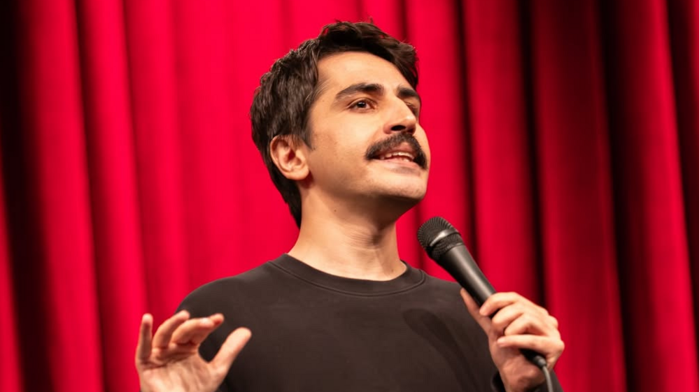 A head-shot posted by a Turkish stand-up comic showing him holding a microphone and standing in front of a red curtain