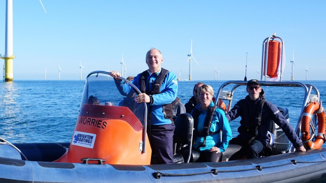 Liberal Democrat leader Sir Ed Davey and the party's energy spokesperson Pippa Heylings in a speedboat during a visit to Rampion Windfarm during the Liberal Democrat Party conference in Brighton. Behind their orange speedboat is a windfarm, set against a blue sky.