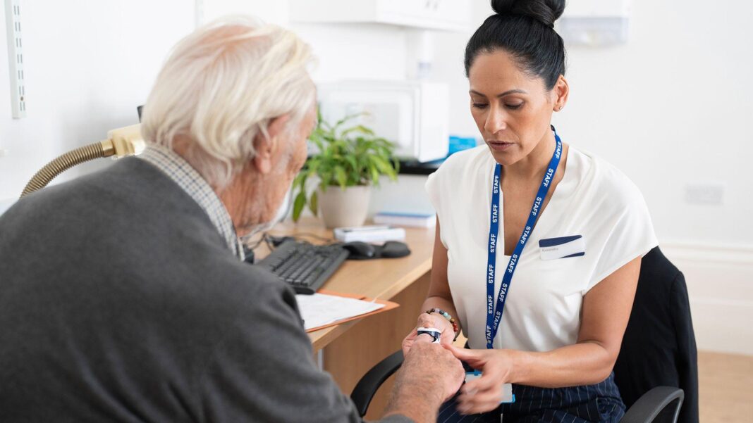AI tools that take notes for GPs could miss vital information, study suggests Stock photo shows a GP with an NHS lanyard around their neck in a GP surgery setting, putting a finger monitor onto a patient during a consultation.
