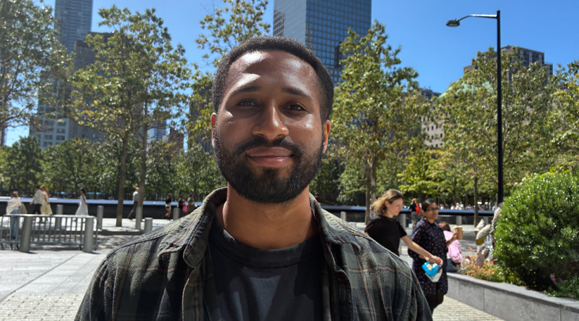 Man with brown hair and a beard smiles at the camera in a park