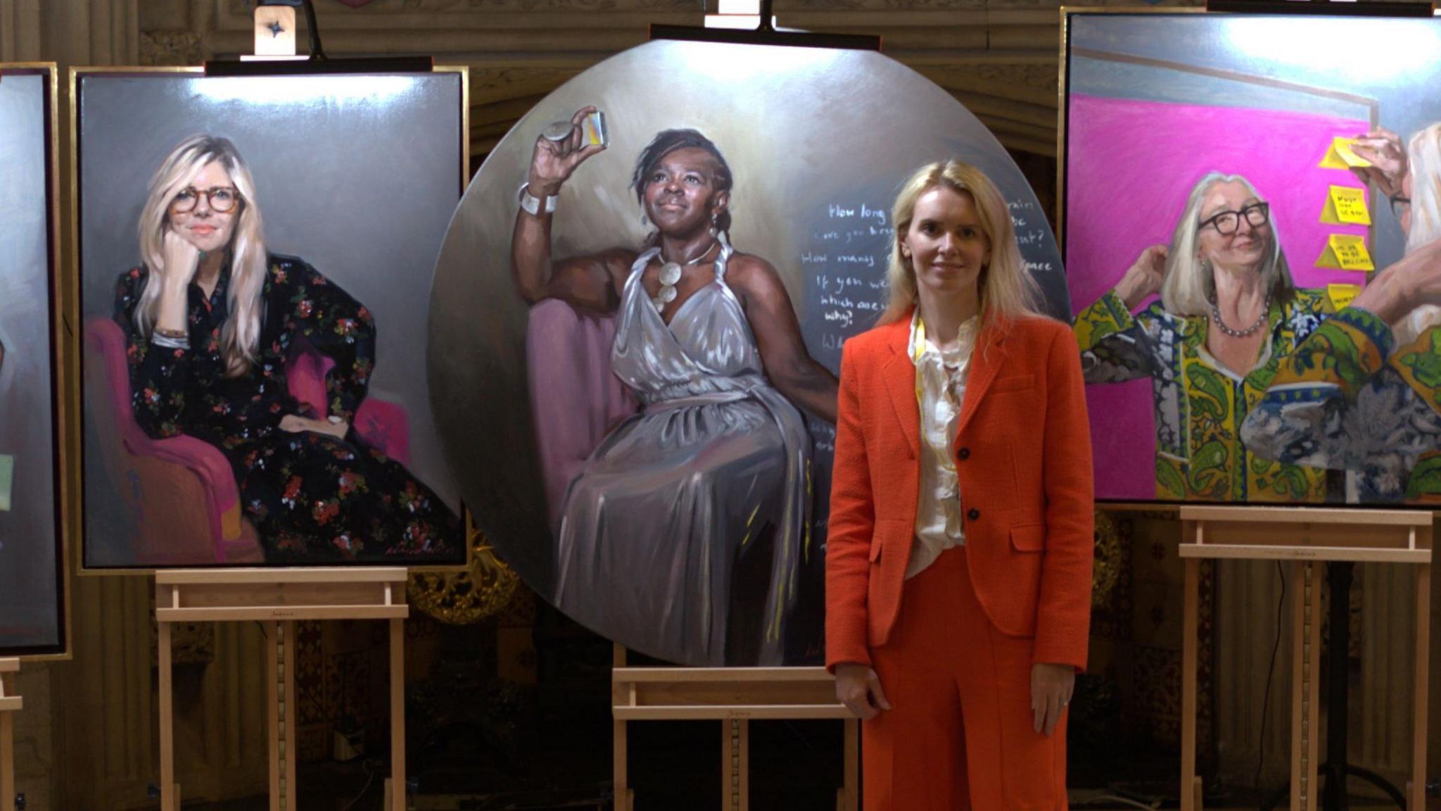 A woman, Caroline De Peyrecave, stood in front of oil portraits of three women.