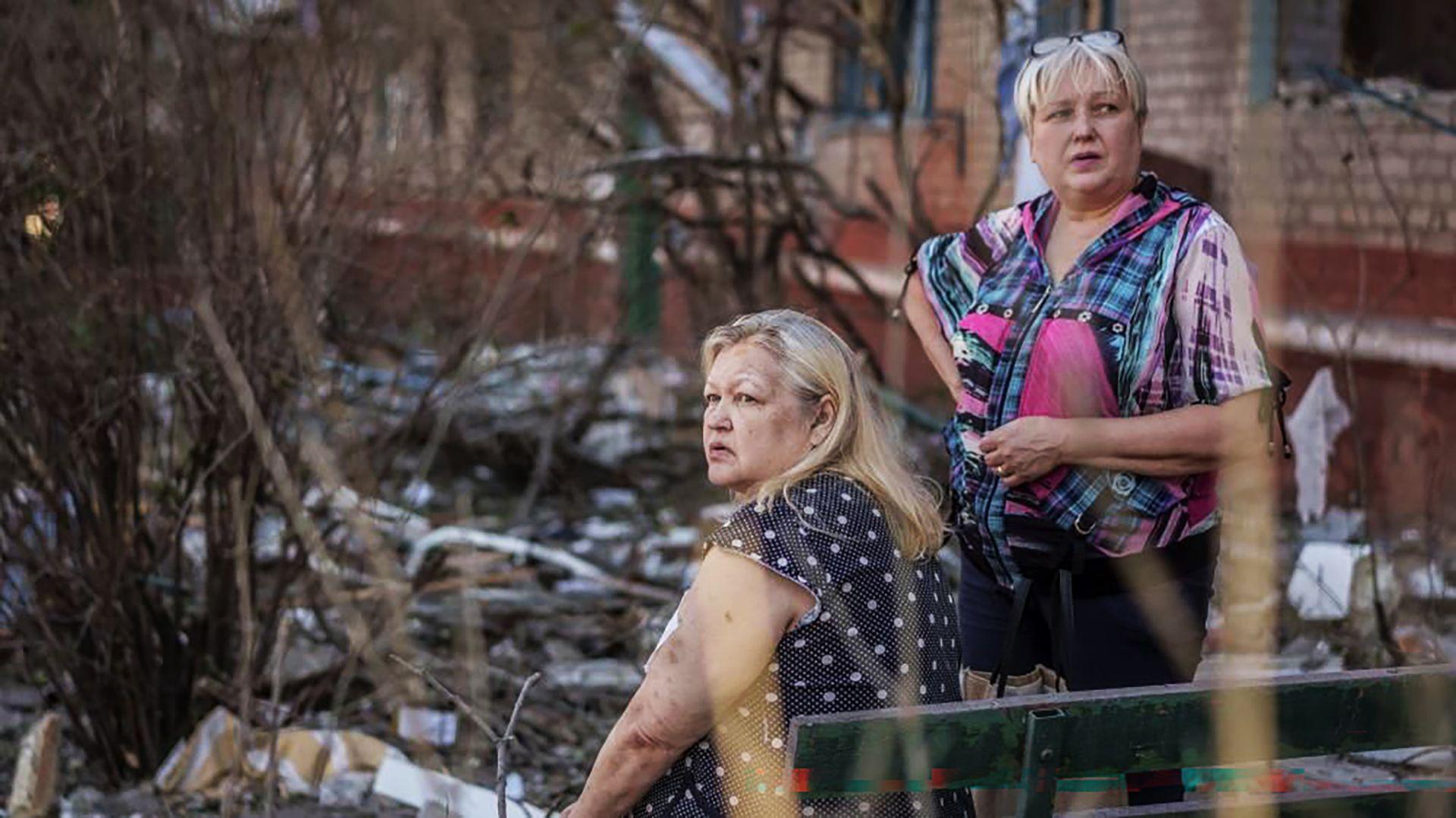 Two middle-aged women stare into the distance amid the rubble from a Russian attack