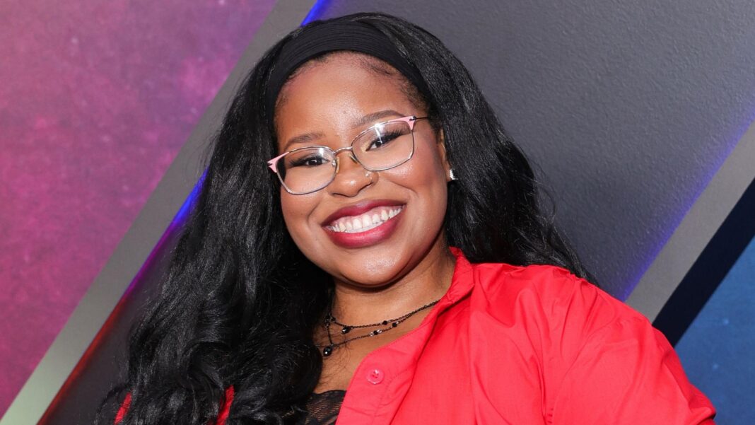 Carla Jeffery grinning in glasses and a red blouse, posing for photos at the world premiere of Disney's Zombies 4: Dawn Of The Vampires at El Capitan Theatre on 8 July, 2025 in Los Angeles.