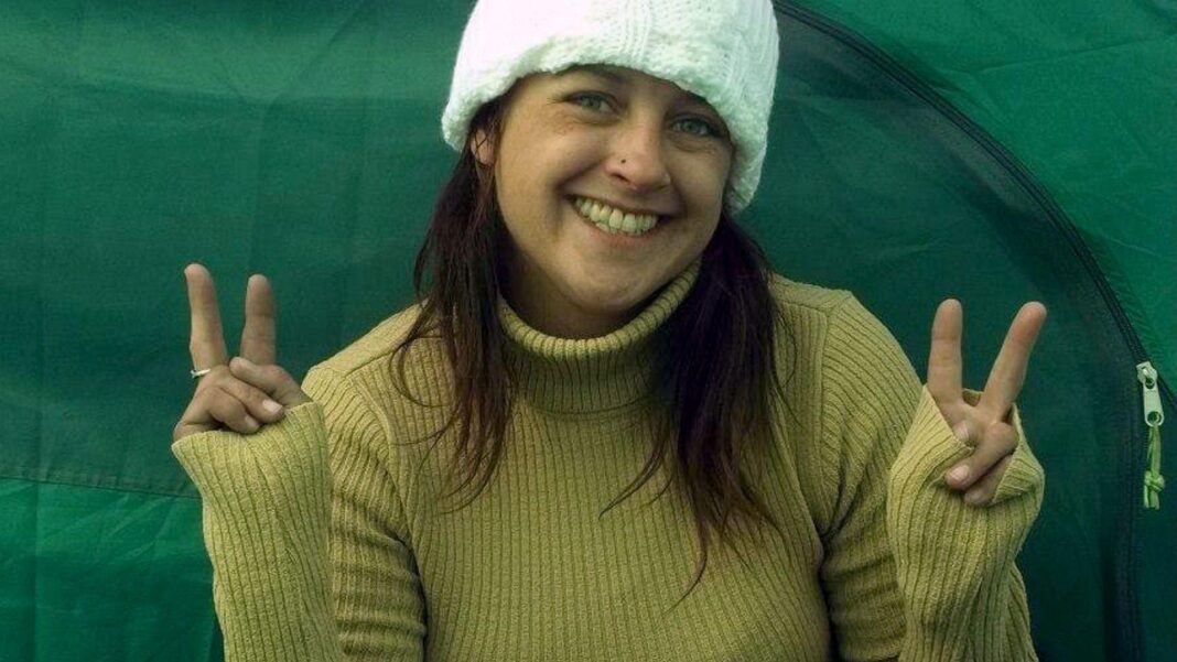 A woman smiles into the camera making peace signs with both hands